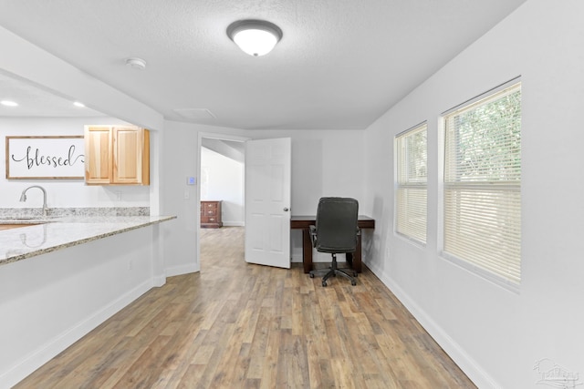 office area with a textured ceiling, a sink, light wood-style flooring, and baseboards