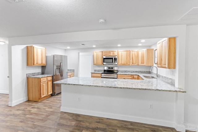 kitchen with light stone counters, light brown cabinetry, appliances with stainless steel finishes, a sink, and a peninsula