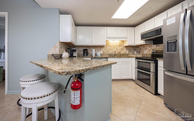 kitchen featuring light tile patterned floors, tasteful backsplash, appliances with stainless steel finishes, and a breakfast bar area