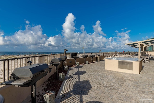 view of patio with a water view, a view of the beach, and exterior kitchen