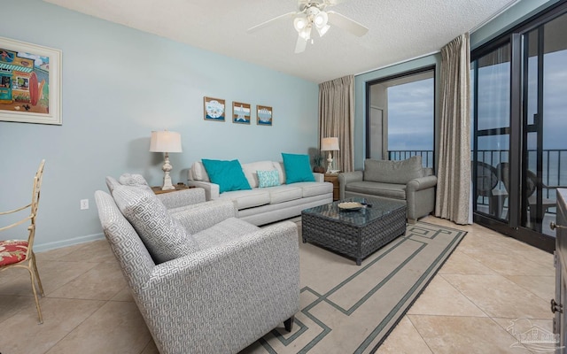 living room featuring a ceiling fan, a textured ceiling, baseboards, and light tile patterned floors