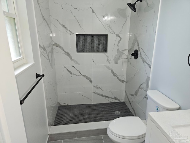 bathroom featuring vanity, toilet, a tile shower, and tile patterned flooring