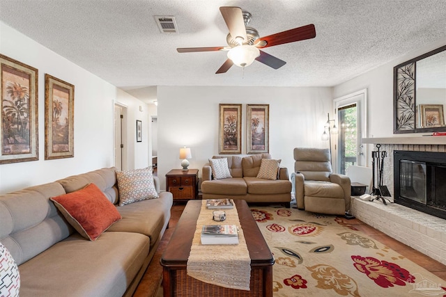 living room featuring a brick fireplace, a textured ceiling, and ceiling fan