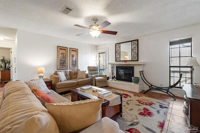 living room featuring light tile patterned flooring, a fireplace, ceiling fan, and a textured ceiling