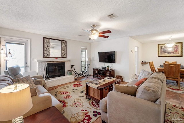 living room featuring a textured ceiling, ceiling fan, a brick fireplace, and plenty of natural light