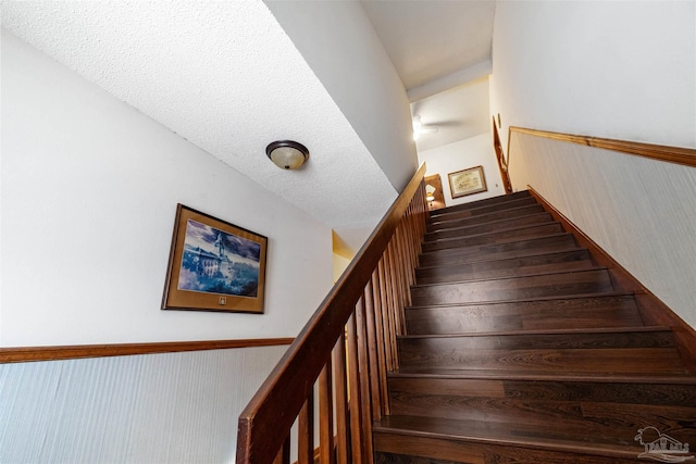 staircase featuring a textured ceiling and wood walls