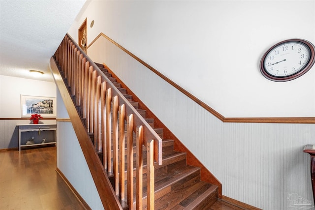 staircase featuring hardwood / wood-style flooring, a textured ceiling, and wooden walls