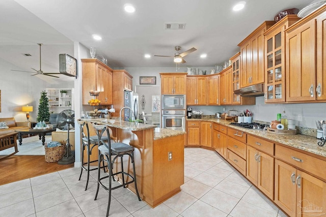 kitchen with a breakfast bar, a kitchen island with sink, light hardwood / wood-style flooring, light stone counters, and stainless steel appliances