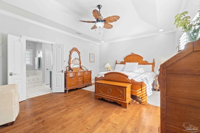 bedroom with a raised ceiling, light wood-type flooring, ensuite bath, and ceiling fan