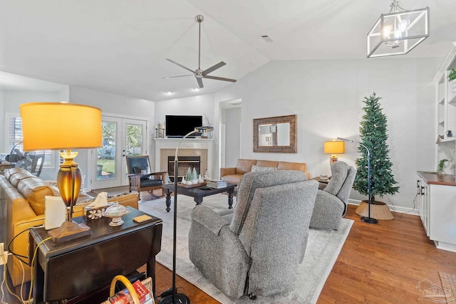 living room with ceiling fan with notable chandelier, light wood-type flooring, french doors, and vaulted ceiling