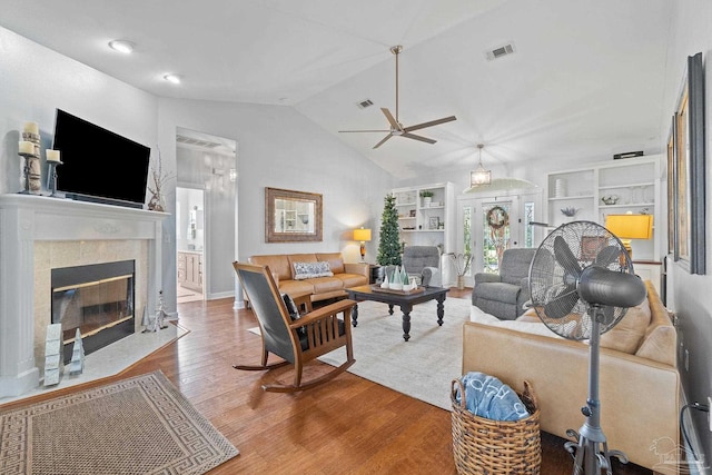 living room featuring hardwood / wood-style flooring, built in shelves, ceiling fan, and vaulted ceiling