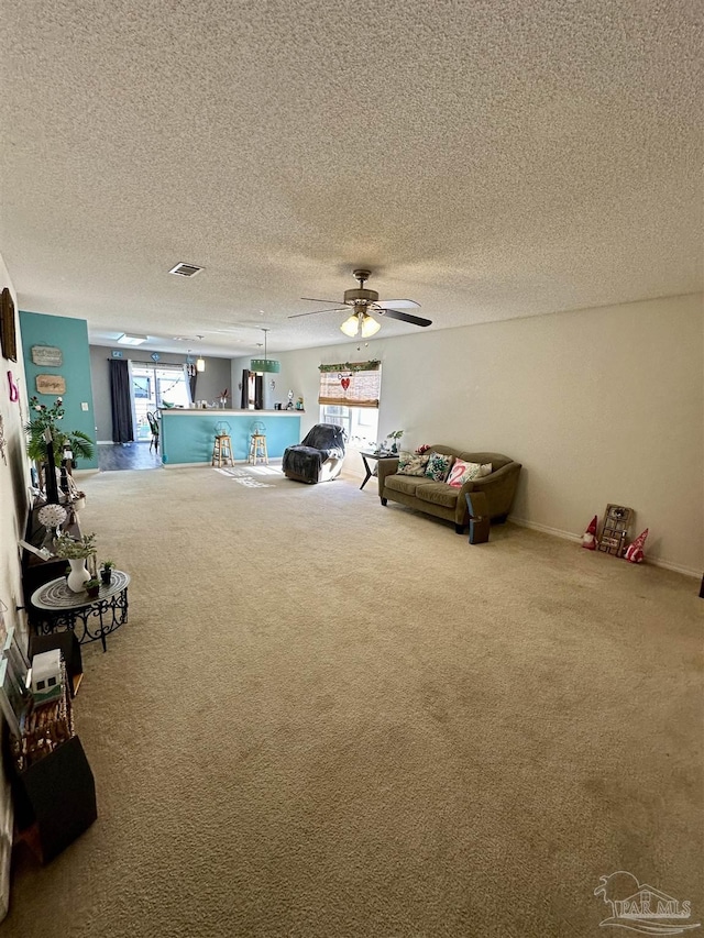 living area featuring carpet flooring, healthy amount of natural light, a textured ceiling, and a ceiling fan