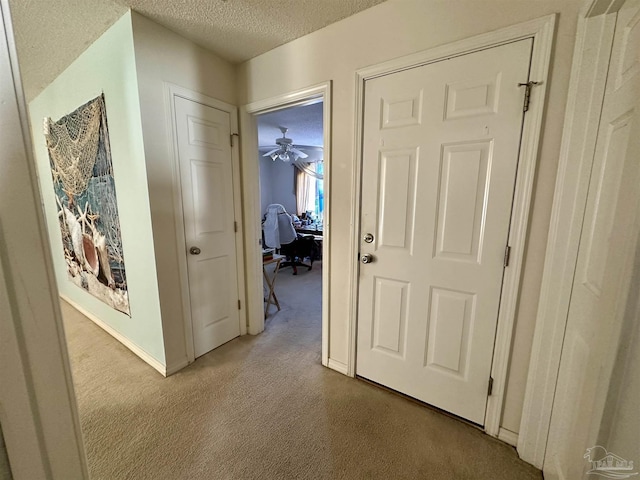 hall with a textured ceiling, carpet flooring, a desk, and baseboards