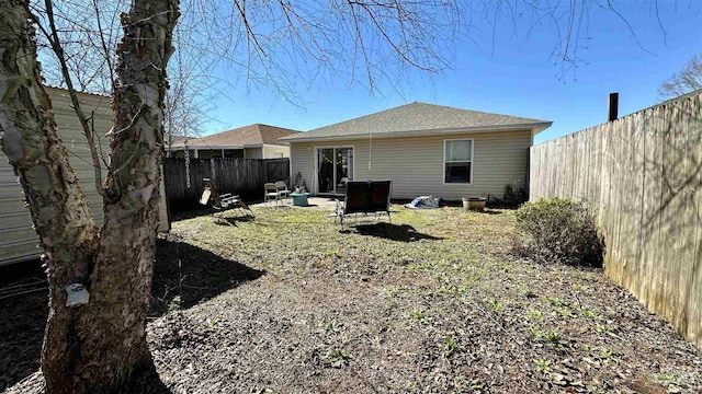 rear view of property featuring a fenced backyard, an outdoor fire pit, and a shingled roof
