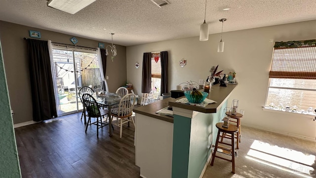 kitchen featuring dark countertops, a textured ceiling, dark wood finished floors, hanging light fixtures, and a breakfast bar area