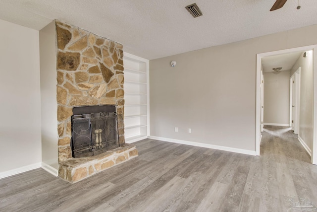 unfurnished living room featuring a fireplace, wood finished floors, visible vents, and a textured ceiling