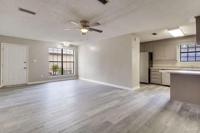 unfurnished living room with visible vents, light wood-style flooring, baseboards, and ceiling fan