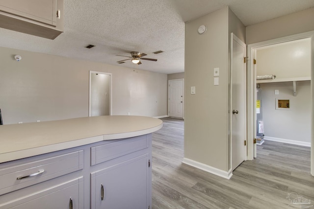 kitchen featuring visible vents, baseboards, ceiling fan, light wood-style flooring, and a textured ceiling