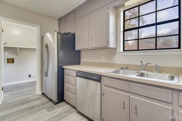 kitchen featuring light wood-type flooring, a sink, stainless steel appliances, light countertops, and baseboards