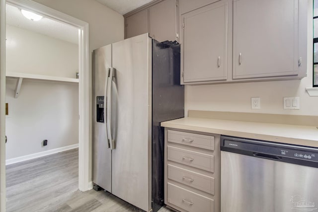 kitchen featuring gray cabinets, stainless steel appliances, light wood-style floors, light countertops, and baseboards