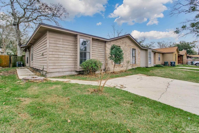 ranch-style home featuring a front lawn, fence, central AC unit, and brick siding