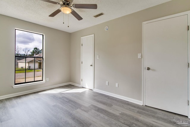 spare room with visible vents, a ceiling fan, a textured ceiling, wood finished floors, and baseboards