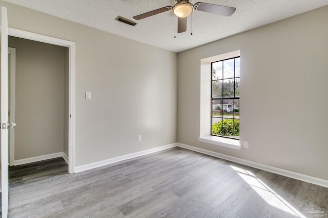 empty room featuring visible vents, a ceiling fan, a textured ceiling, wood finished floors, and baseboards