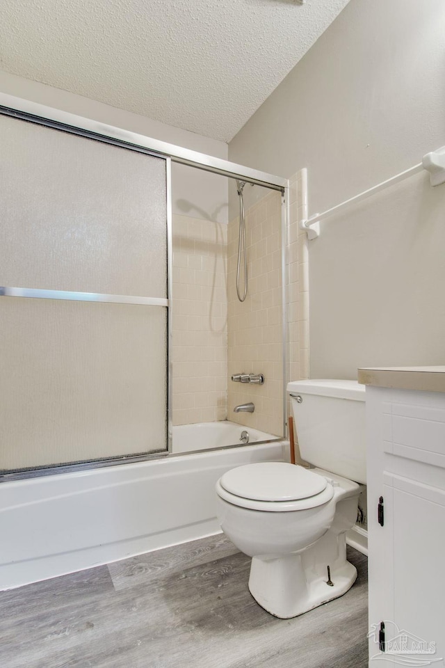 bathroom with toilet, wood finished floors, bath / shower combo with glass door, and a textured ceiling