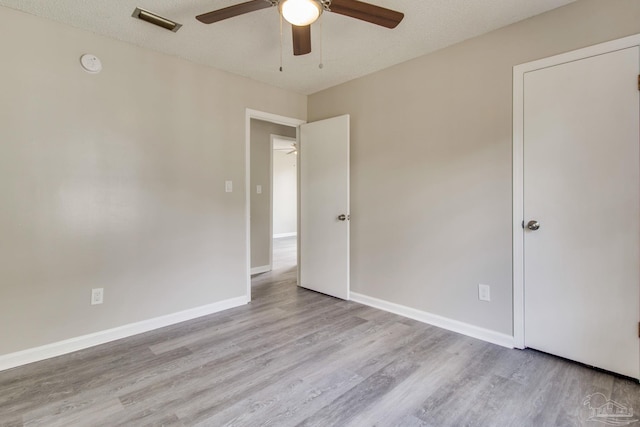 unfurnished room featuring a textured ceiling, wood finished floors, visible vents, and baseboards