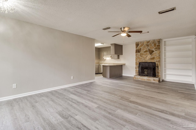 unfurnished living room featuring light wood-type flooring, visible vents, a textured ceiling, and a stone fireplace