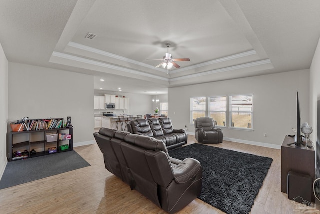 living room featuring visible vents, ornamental molding, a ceiling fan, a tray ceiling, and light wood-style floors