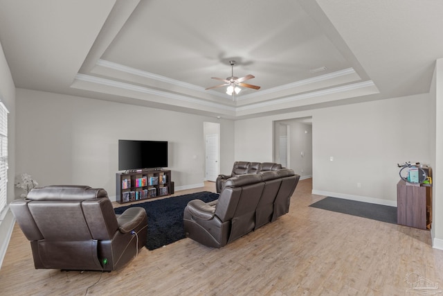 living room featuring a tray ceiling, crown molding, a ceiling fan, and light wood finished floors