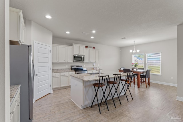 kitchen with a kitchen bar, an island with sink, light wood-type flooring, and appliances with stainless steel finishes