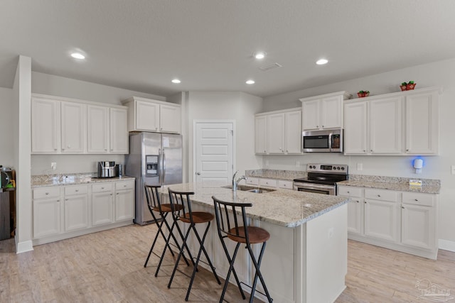 kitchen with a kitchen bar, visible vents, a sink, stainless steel appliances, and light wood finished floors