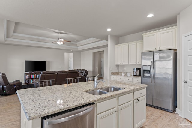 kitchen with a sink, open floor plan, a tray ceiling, appliances with stainless steel finishes, and a kitchen island with sink