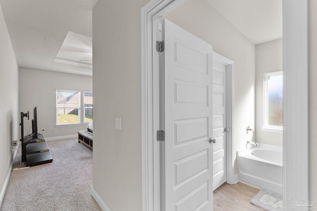 bathroom with a tray ceiling, baseboards, a bath, and ensuite bathroom