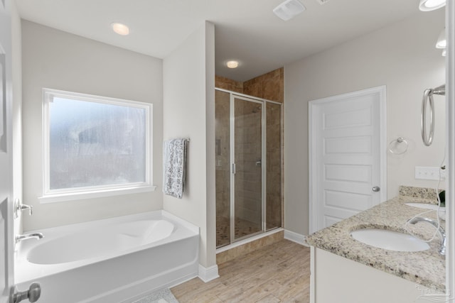 bathroom featuring wood finished floors, double vanity, a stall shower, a sink, and a garden tub