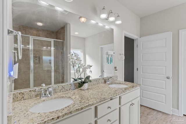 full bath featuring a shower stall, wood finished floors, double vanity, and a sink