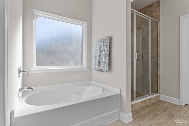 bathroom with a stall shower, baseboards, a garden tub, and wood finished floors