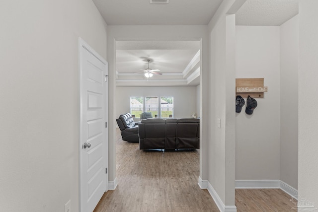 hallway with baseboards, a raised ceiling, and wood finished floors