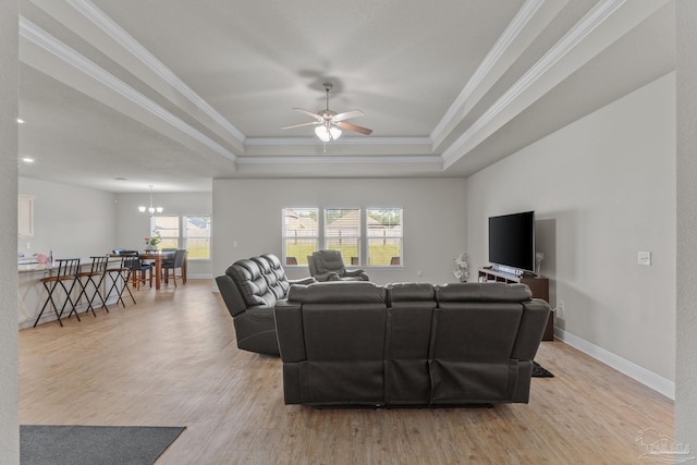 living room featuring crown molding, baseboards, light wood-type flooring, a tray ceiling, and ceiling fan with notable chandelier