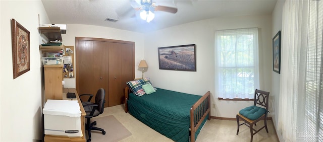 bedroom featuring a textured ceiling, ceiling fan, light carpet, and a closet