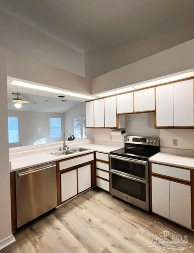 kitchen with light countertops, appliances with stainless steel finishes, light wood-style floors, white cabinets, and a sink