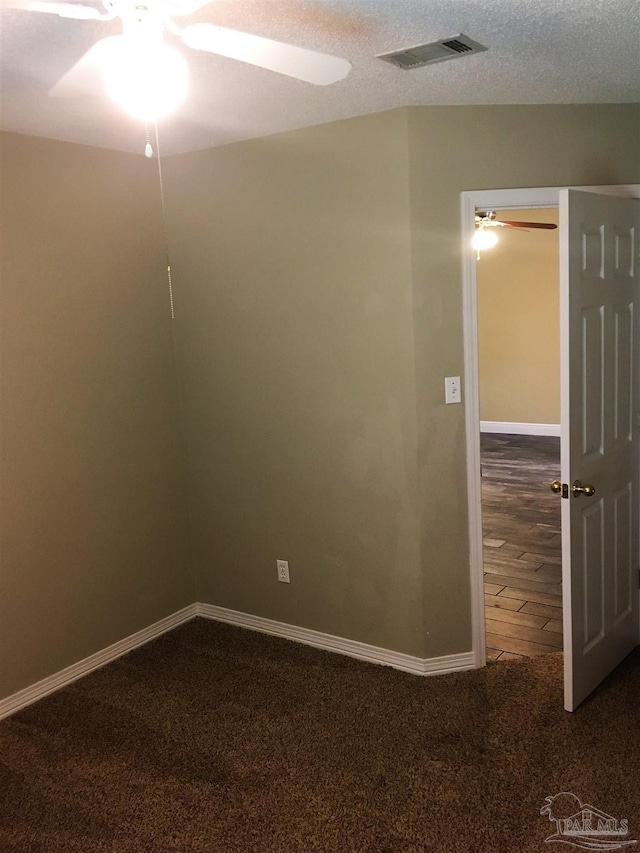 spare room with a ceiling fan, baseboards, visible vents, a textured ceiling, and dark carpet