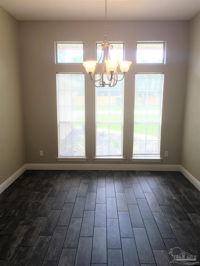 unfurnished dining area featuring a chandelier, baseboards, a healthy amount of sunlight, and dark wood-style floors