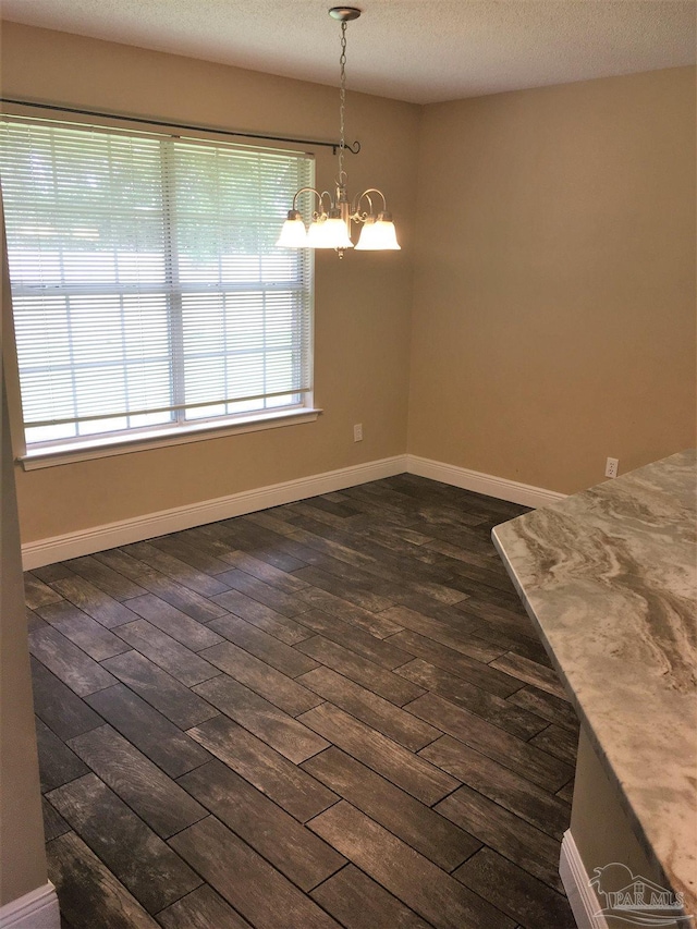 unfurnished dining area featuring an inviting chandelier, dark wood-type flooring, baseboards, and a textured ceiling