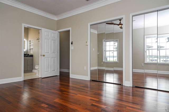 unfurnished bedroom with ornamental molding, two closets, and dark hardwood / wood-style flooring