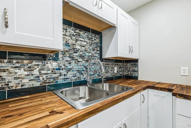 kitchen with wood counters, a sink, tasteful backsplash, and white cabinets