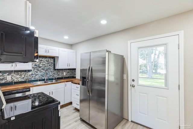 kitchen with wooden counters, stainless steel refrigerator with ice dispenser, a sink, black range with electric cooktop, and white cabinetry