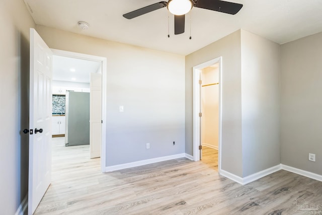 unfurnished bedroom featuring freestanding refrigerator, light wood-style floors, baseboards, and ceiling fan